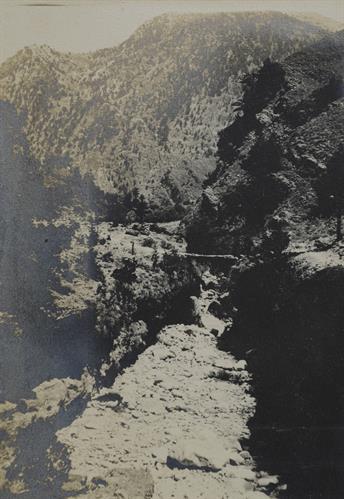 Chania, Crete. Dry riverbed of a torrent in a mountain. A wooden bridge connects the two sides. Photograph, 1909.