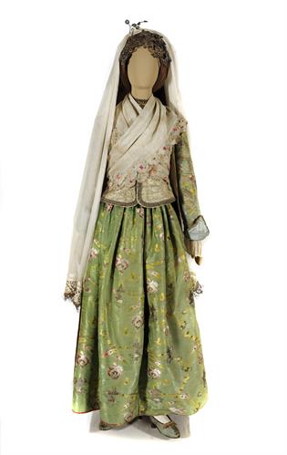Rare festal costume from Ios island. It consists of a white gossamer silk tunic with broad lace decoration, a skirt of luxurious silk material, a waistcoat and a long tight-fitting coat (&quot;binisi&quot;). The headgear (&quot;kourli&quot;) is made up of a kerchief, a white