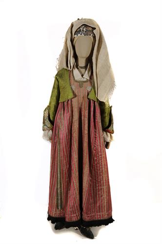 Festal costume from Lemnos island. It consists of the breeches, a white cotton-silk tunic, a silk dress decorated with gold braid and black woolen fringes at the hem and a silk waistcoat. The headgear is made up of a red cap, a print kerchief and a fine h